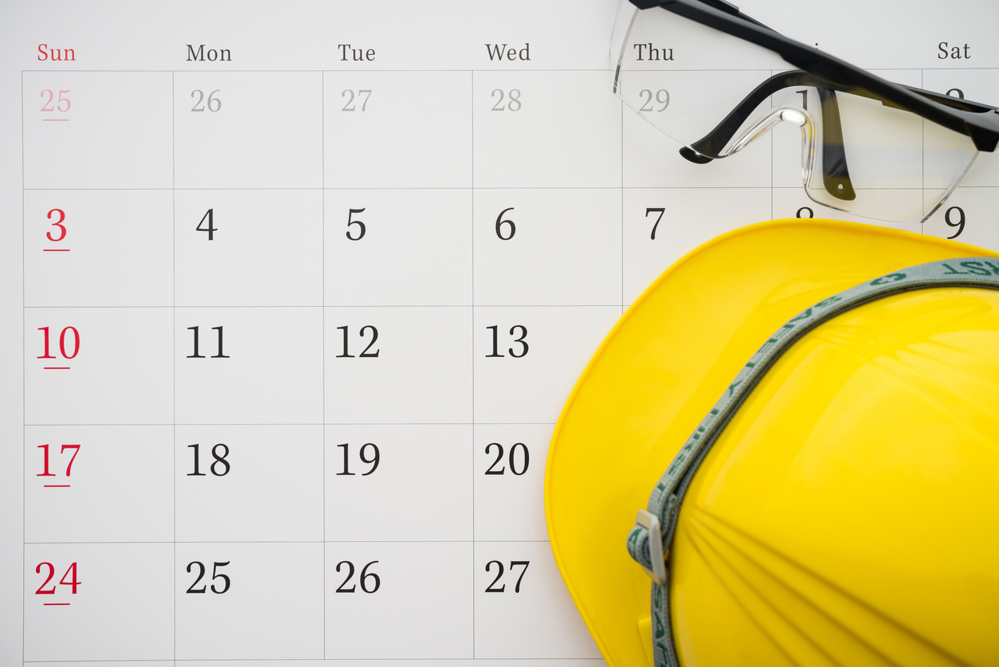 Flat lay of safety glass and yellow worker helmet on blank white calendar background copy space. Payday, working or training schedule for worker or employee, labor day, holiday and so on concept