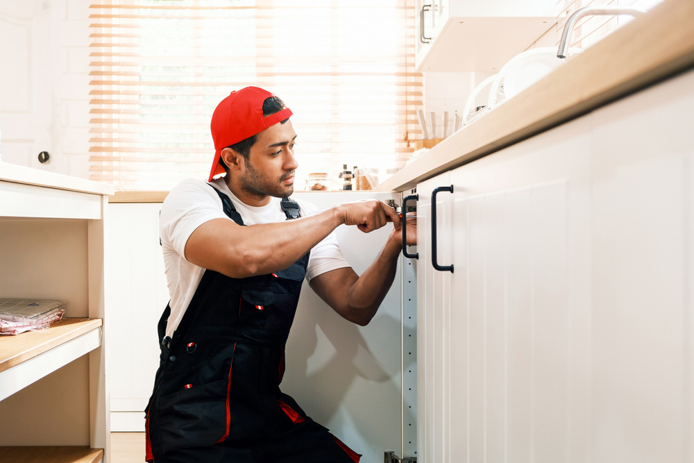 Professional handyman in uniform installing a kitchen cabinet handle. Home repair, renovation, and maintenance services concept. Skilled worker using a screwdriver for cabinet fitting